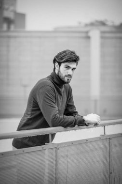 Yakışıklı, siyah saçlı, metal korkuluklara yaslanmış, kırmızı kazaklı bir İtalyan. Yüksek kalite fotoğraf