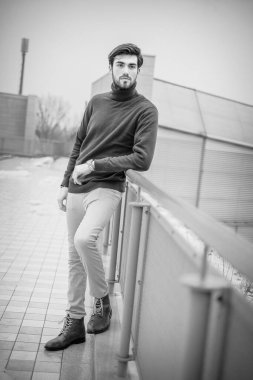 Yakışıklı, siyah saçlı, metal korkuluklara yaslanmış, kırmızı kazaklı bir İtalyan. Yüksek kalite fotoğraf