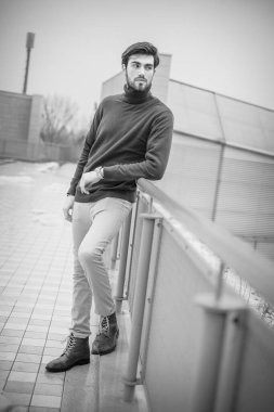 Yakışıklı, siyah saçlı, metal korkuluklara yaslanmış, kırmızı kazaklı bir İtalyan. Yüksek kalite fotoğraf