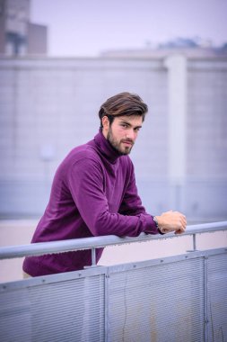 Yakışıklı, siyah saçlı, metal korkuluklara yaslanmış, kırmızı kazaklı bir İtalyan. Yüksek kalite fotoğraf