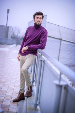 Yakışıklı, siyah saçlı, metal korkuluklara yaslanmış, kırmızı kazaklı bir İtalyan. Yüksek kalite fotoğraf