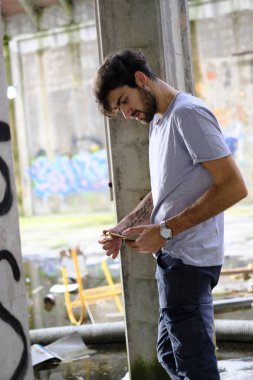 Dejenere olmuş terk edilmiş fabrikadaki yakışıklı siyah saçlı İtalyan adam telefonu kullanıyor. Yüksek kalite fotoğraf