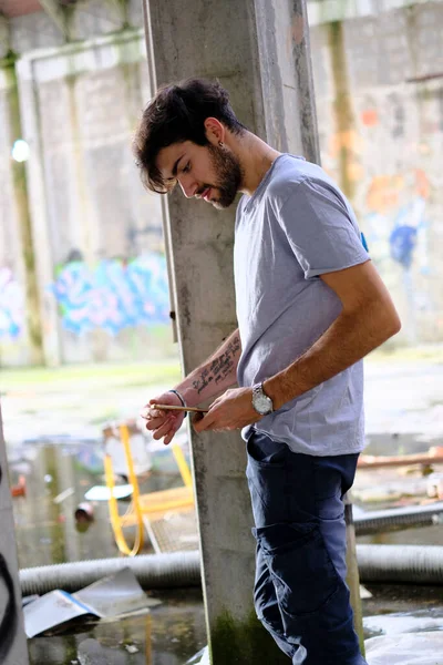 Dejenere olmuş terk edilmiş fabrikadaki yakışıklı siyah saçlı İtalyan adam telefonu kullanıyor. Yüksek kalite fotoğraf