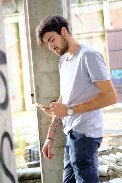 Dejenere olmuş terk edilmiş fabrikadaki yakışıklı siyah saçlı İtalyan adam telefonu kullanıyor. Yüksek kalite fotoğraf