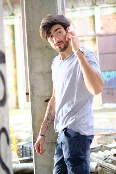 Dejenere olmuş terk edilmiş fabrikadaki yakışıklı siyah saçlı İtalyan adam telefonu kullanıyor. Yüksek kalite fotoğraf