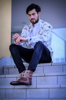 Yakışıklı, siyah saçlı, beyaz ceketli, merdivenlerde oturan adam. Yüksek kalite fotoğraf