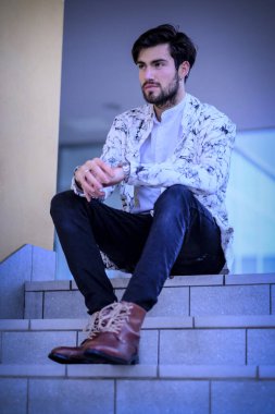 Yakışıklı, siyah saçlı, beyaz ceketli, merdivenlerde oturan adam. Yüksek kalite fotoğraf