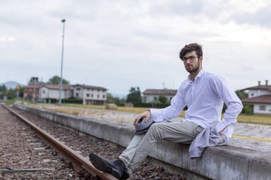 Yakışıklı, siyah saçlı İtalyan çocuk istasyondaki tren istasyonunda oturuyor. Yüksek kalite fotoğraf