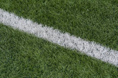 Green synthetic grass sports field with white line shot from above. Sports background for product display, banner, or mockup. High quality photo