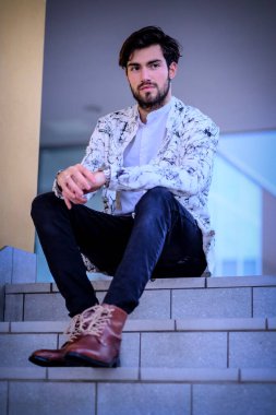 Beyaz merdivenlerde oturan yakışıklı, siyah saçlı İtalyan adam. Yüksek kalite fotoğraf