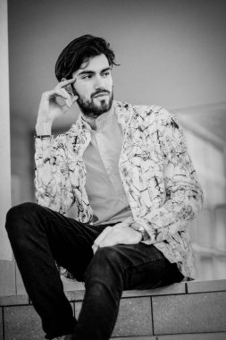 handsome Italian dark-haired guy sitting on white stairs. High quality photo