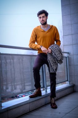 Yakışıklı, siyah saçlı, metal korkuluklara yaslanmış bir çocuk. Yüksek kalite fotoğraf