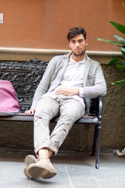 Spor ceketli yakışıklı, koyu renk saçlı adam bankta oturuyor. Yüksek kalite fotoğraf