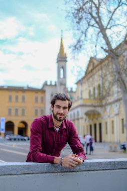 Şehir merkezinde koyu kırmızı tişörtlü yakışıklı, koyu renk saçlı İtalyan adam. Yüksek kalite fotoğraf