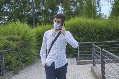 handsome dark-haired Italian boy walks with anti-covid mask and talks on the phone. High quality photo
