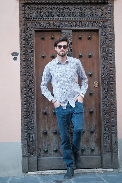 handsome Italian guy poses in front of an ancient door in a shirt. High quality photo