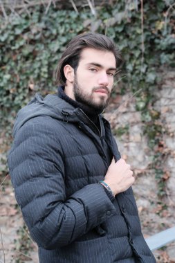 Yakışıklı, siyah saçlı, kışlık ceketli, metal korkuluklara yaslanmış bir çocuk. Yüksek kalite fotoğraf