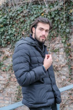 Yakışıklı, siyah saçlı, kışlık ceketli, metal korkuluklara yaslanmış bir çocuk. Yüksek kalite fotoğraf