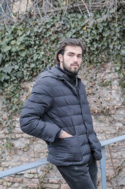 Yakışıklı, siyah saçlı, kışlık ceketli, metal korkuluklara yaslanmış bir çocuk. Yüksek kalite fotoğraf