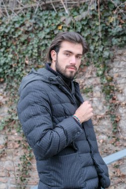 Yakışıklı, siyah saçlı, kışlık ceketli, metal korkuluklara yaslanmış bir çocuk. Yüksek kalite fotoğraf