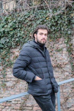 Yakışıklı, siyah saçlı, kışlık ceketli, metal korkuluklara yaslanmış bir çocuk. Yüksek kalite fotoğraf