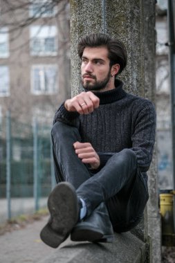 Yakışıklı İtalyan siyah saçlı çocuk alçak duvarda oturuyor. Yüksek kalite fotoğraf