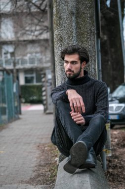 Yakışıklı İtalyan siyah saçlı çocuk alçak duvarda oturuyor. Yüksek kalite fotoğraf