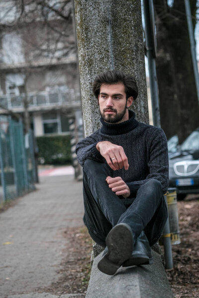portrait handsome Italian dark-haired boy sitting on low wall. High quality photo