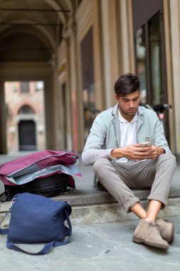 Yakışıklı, siyah saçlı İtalyan adam akıllı telefon kullanırken şehir merdivenlerinde oturuyor. Yüksek kalite fotoğraf