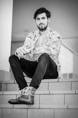 Yakışıklı, siyah saçlı, beyaz ceketli, merdivenlerde oturan adam. Yüksek kalite fotoğraf