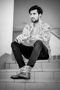 Yakışıklı, siyah saçlı, beyaz ceketli, merdivenlerde oturan adam. Yüksek kalite fotoğraf