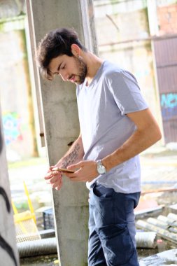 Dejenere olmuş terk edilmiş fabrikadaki yakışıklı siyah saçlı İtalyan adam telefonu kullanıyor. Yüksek kalite fotoğraf