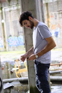 Dejenere olmuş terk edilmiş fabrikadaki yakışıklı siyah saçlı İtalyan adam telefonu kullanıyor. Yüksek kalite fotoğraf