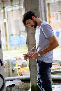 Dejenere olmuş terk edilmiş fabrikadaki yakışıklı siyah saçlı İtalyan adam telefonu kullanıyor. Yüksek kalite fotoğraf