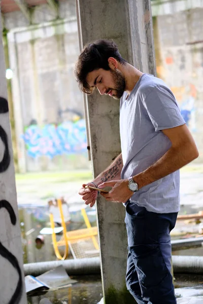 Dejenere olmuş terk edilmiş fabrikadaki yakışıklı siyah saçlı İtalyan adam telefonu kullanıyor. Yüksek kalite fotoğraf