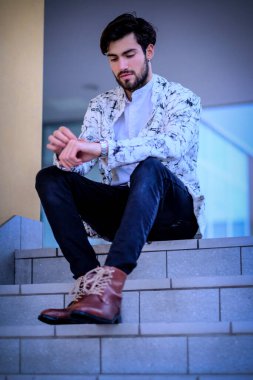 Beyaz merdivenlerde oturan yakışıklı, siyah saçlı İtalyan adam. Yüksek kalite fotoğraf