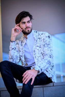 Yakışıklı, siyah saçlı, beyaz ceketli, merdivenlerde oturan adam. Yüksek kalite fotoğraf