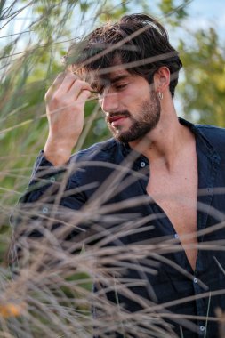 handsome Italian dark-haired guy with shirt in the dry grass. High quality photo