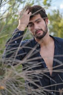 Kuru çimenlerde gömleği olan yakışıklı, siyah saçlı bir İtalyan. Yüksek kalite fotoğraf