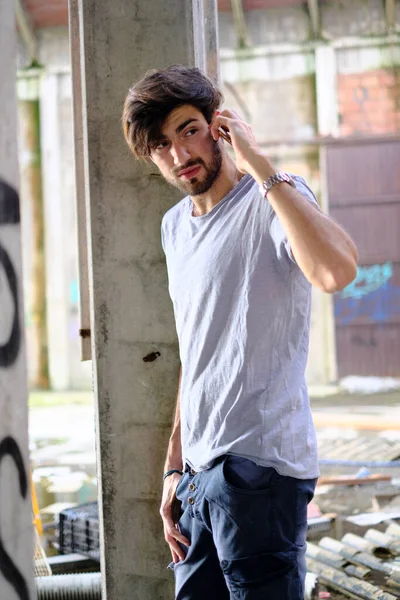 Dejenere olmuş terk edilmiş fabrikadaki yakışıklı siyah saçlı İtalyan adam telefonu kullanıyor. Yüksek kalite fotoğraf