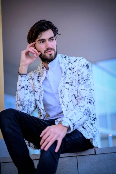 Yakışıklı, siyah saçlı, beyaz ceketli, merdivenlerde oturan adam. Yüksek kalite fotoğraf