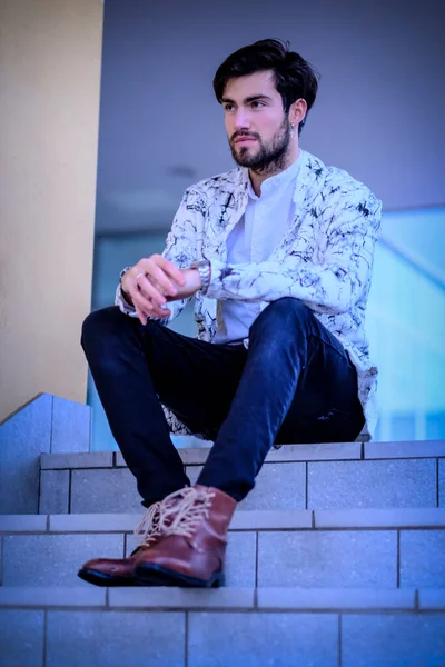 Yakışıklı, siyah saçlı, beyaz ceketli, merdivenlerde oturan adam. Yüksek kalite fotoğraf