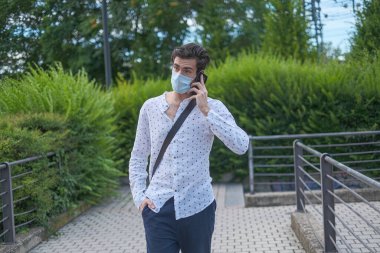 handsome dark-haired Italian boy walks with anti-covid mask and talks on the phone. High quality photo