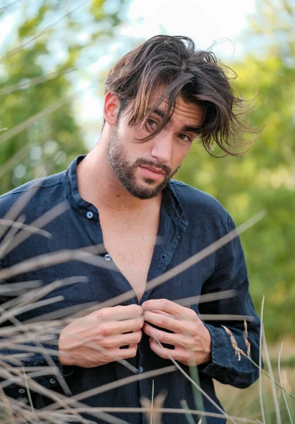 Kuru çimenlerde gömleği olan yakışıklı, siyah saçlı bir İtalyan. Yüksek kalite fotoğraf