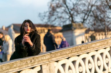beautiful Italian girl with red dress and black jacket on the bridge in the square in Padua. High quality photo