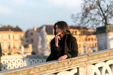 beautiful Italian girl with red dress and black jacket on the bridge in the square in Padua. High quality photo