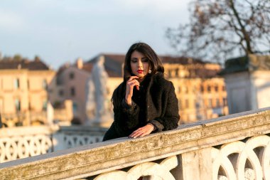 beautiful Italian girl with red dress and black jacket on the bridge in the square in Padua. High quality photo
