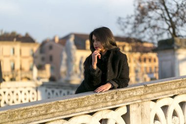beautiful Italian girl with red dress and black jacket on the bridge in the square in Padua. High quality photo