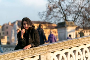 beautiful Italian girl with red dress and black jacket on the bridge in the square in Padua. High quality photo
