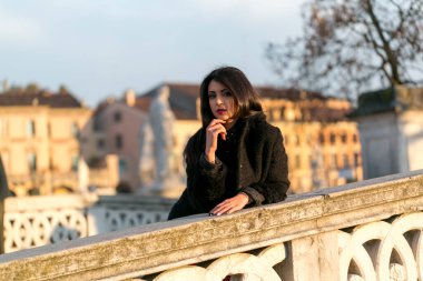 beautiful Italian girl with red dress and black jacket on the bridge in the square in Padua. High quality photo